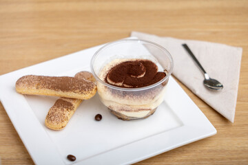 Delicious tiramisu dessert served in a glass jar, showcasing creamy layers of mascarpone cheese and coffee-soaked ladyfingers. Accompanied by a jar of extra ladyfingers