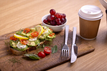 A delicious breakfast plate featuring poached eggs, avocado toast with lemon and tomato, a fresh salad, and a small bunch of grapes. Perfect for healthy eating and gourmet food themes.