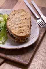 A wholesome sandwich filled with spinach, corn, and cheese, served on whole grain bread with a side of fresh green salad. The sandwich is placed on a rustic white plate with salt and pepper shakers