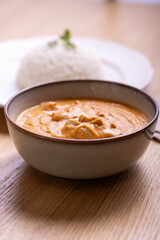 Delicious bowl of creamy butter chicken served with a mound of steamed white rice garnished with cilantro on a white plate, accompanied by a refreshing orange juice in a plastic cup. 