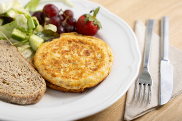 A delicious breakfast plate featuring a golden-brown omelette, two slices of whole grain bread, a fresh mixed green salad, red grapes, and a ripe strawberry. A nutritious and balanced meal ideal.