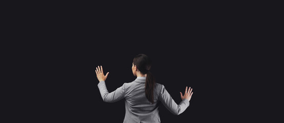 A woman in a blazer stands facing a black background, her hands outstretched as if she is interacting with an invisible screen.