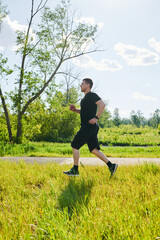 A male athlete is training on the sports ground outside. Caucasian male athlete jogging outdoors in a summer park