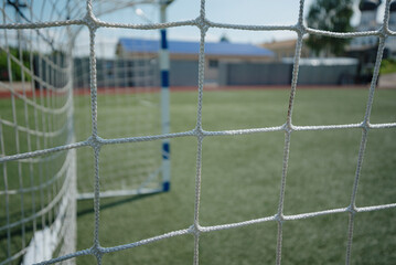 net of football goal, green artificial grass, football field, sunny summer day, selective focus