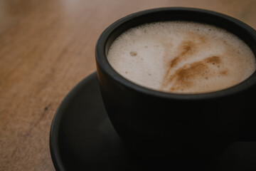 A black coffee cup, mug stands on an old wooden table. Aromatic tasty cappuccino or cocoa in a cafe. Aromatic and hot morning beverage in cafeteria. 