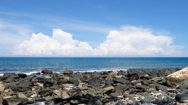 A sunny day on a rocky beach with calm waves against a backgrounds of blue sky and sea in Manatuto, Timor Leste.
