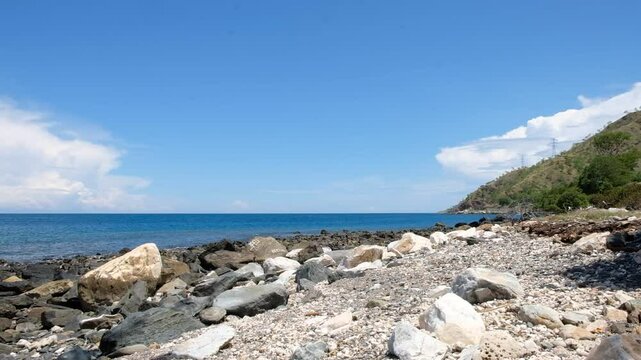 A sunny day on a rocky beach with calm waves against a backgrounds of blue sky and sea in Manatuto, Timor Leste.
