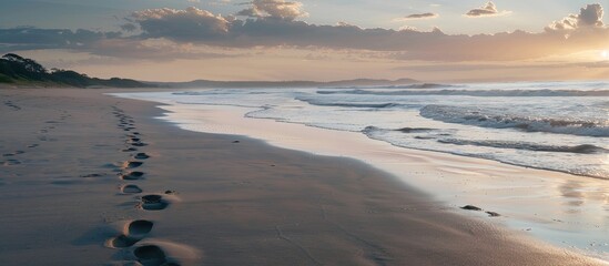 Footprints leaving a trail on the sandy beach at dusk with a serene background, perfect for a copy space image.