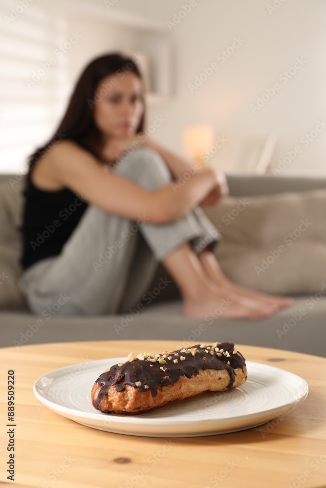 Poster Eating disorder. Woman sitting on sofa indoors, focus on eclair