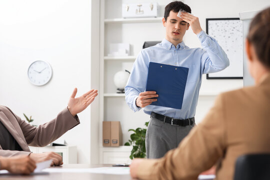 Man with clipboard feeling embarrassed during business meeting in office