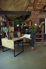 Promoting healthy and active lifestyle in modern office setting. Woman standing at her desk and doing stretching activity. Concept of office life, balance between work and sport, business
