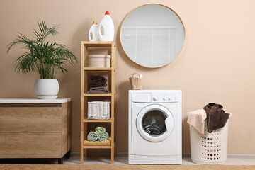 Stylish laundry room interior with washing machine, furniture, detergents and houseplant