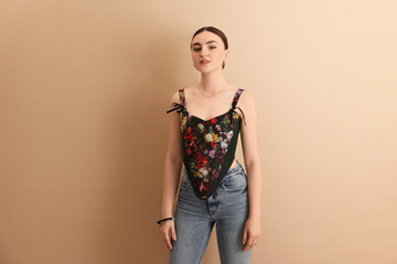 Beautiful young woman in stylish corset on beige background