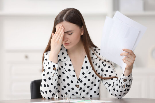 Embarrassed woman with documents at table in office