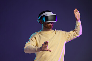 Smiling man using virtual reality headset on dark purple background