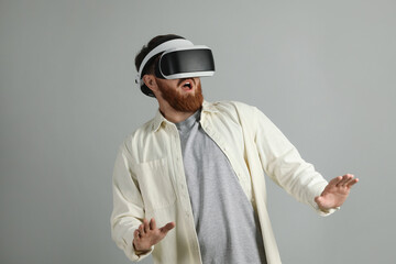 Emotional man using virtual reality headset on grey background