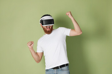 Emotional man using virtual reality headset on pale green background