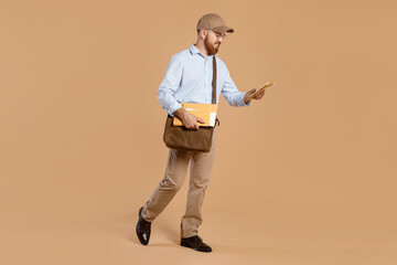 Happy young postman with leather bag delivering letters on brown background