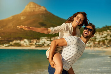 Portrait, couple and piggyback by ocean for love, commitment and bonding on summer vacation for honeymoon. Man, woman and freedom on beach for romantic holiday, airplane and weekend with energy.