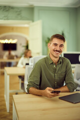 A man working at the co-working space, using his mobile phone, smiling for the camera.