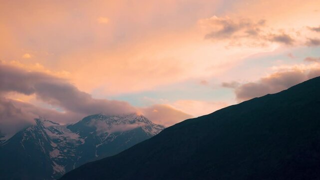 4K shot of orange clouds above the snowy Himalayan mountain peak of the Lahaul Valley as seen from Keylong in Himachal Pradesh, India during the sunset. Beautiful dramatic sky during the sunset.