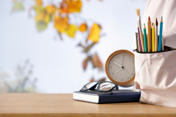 School supplies and schoolbag on wooden school desk. Blurred classroom background and copy space...