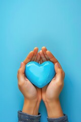 A person is holding a blue heart in their hands. The heart is made of a material that looks like it is made of plastic