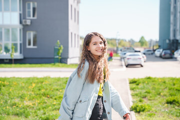 A young teenage girl walks along an empty street between high-rise buildings. Teenage high school student girl with backpack on city street