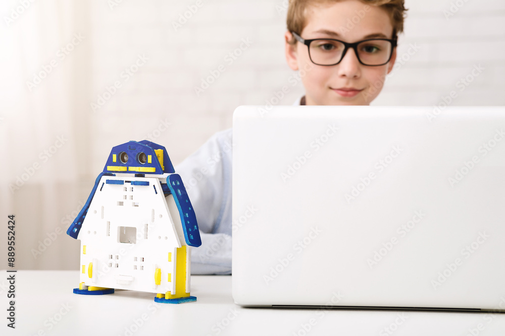 Poster a young boy wearing glasses is sitting at a desk, using a laptop computer. he has a colorful, roboti