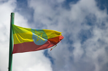 The Ethiopian flag, with its green, yellow, and red stripes and central emblem, waves proudly in the wind against a cloudy sky