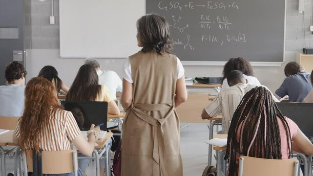 Group of diverse teenage students in class taking an exam while the teacher watches them. High school, university.