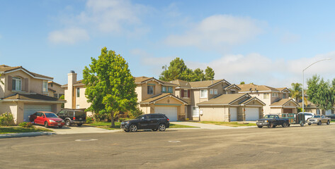 Obraz premium Beautiful houses with nicely landscaped front the yard, and cars parked on a sidewalk.