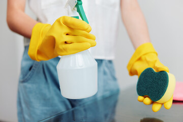 Woman in yellow gloves cleaning glass table with sponge and cleaning solution bottle