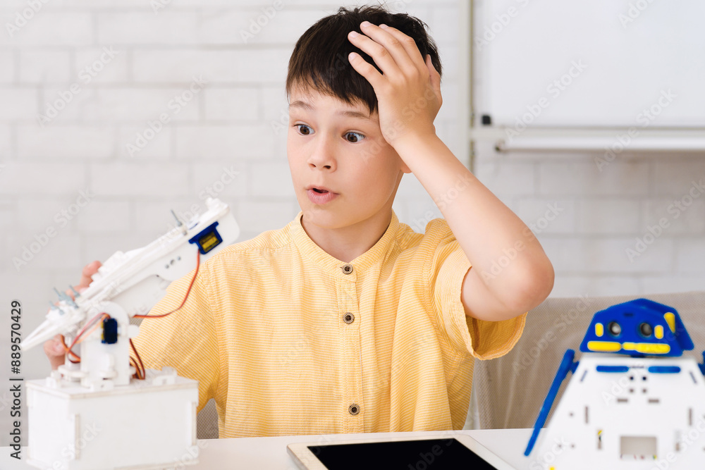 Poster a young boy sits at a table, looking at his robot arm project with a frustrated expression. he has o