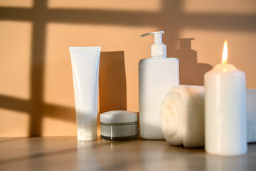White containers, white towel and burning candle. On a beige background.
