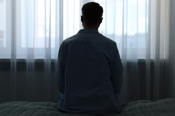 Loneliness concept. Sad man sitting on bed at home, back view
