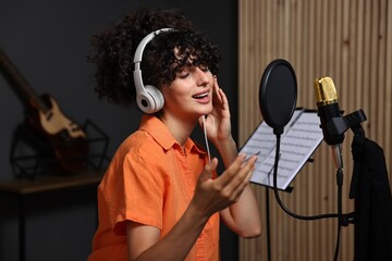 Vocalist with headphones singing into microphone in professional record studio