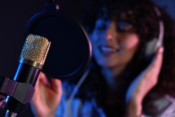 Woman singing into microphone in professional record studio, selective focus