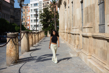 beautiful young latin woman with black eyes and dark, long curly hair walks through the centre of Seville next to the archive of the india and some 15th century stone columns. she is in Andalusia.