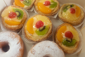 Danish fruit tarts and donuts in a box. Top view of many custard pastries topped with fruit.