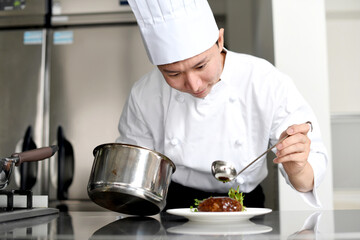 料理を皿に盛る若いアジア人の男性調理師