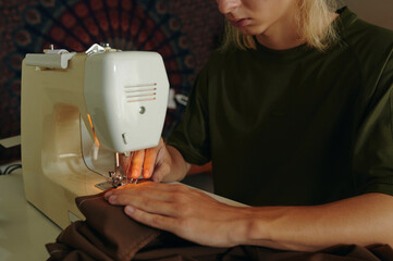 Young tailor sewing clothing on sewing machine in studio