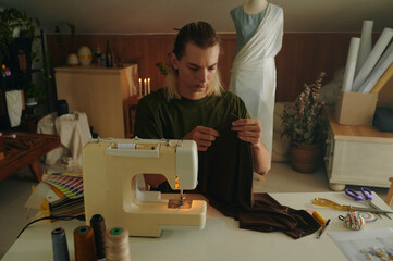 Fashion designer working with clothes while sitting at his workplace with sewing machine