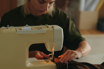 Young fashion designer working with sewing machine and sewing new dress for model