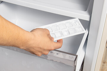 Man puts an ice mold with water in the freezer. Making ice cubes