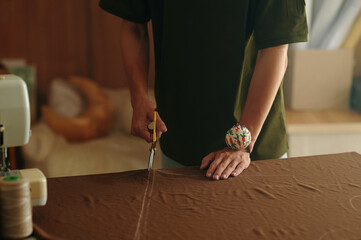 Close-up of tailor standing at table and cutting fabric with scissors for details for further sewing