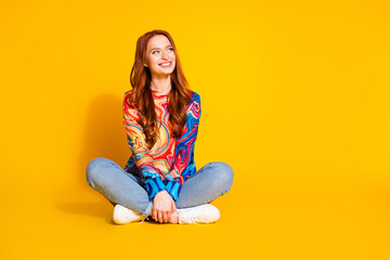 Full body photo of attractive young woman sit floor look empty space dressed stylish colorful clothes isolated on orange color background