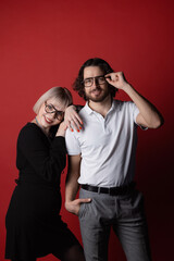 Man and woman fashionable wearing glasses standing on background of red wall in studio. Concept fashion clinic optical ophthalmologist.