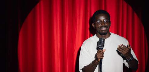 African american man comic with old microphone on theater stage on red curtains background. Concept...