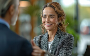 Fototapeta premium A happy, mature Latina businesswoman, wearing a blazer and necklace, smiles as she converses with a colleague